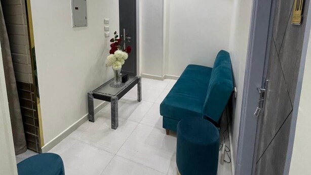 A modern living room with a sofa, a small table with flowers, and a door with a number plate. - Amadeus familias (Giza)