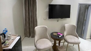 A hotel room with two armchairs, a small table, a TV mounted on the wall, and an air conditioning unit. - Amadeus familias (Giza)