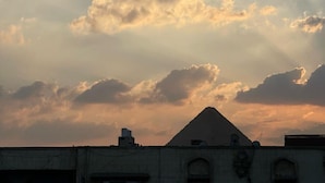 A building with a pyramid-shaped roof, surrounded by clouds. - Amadeus familias (Giza)