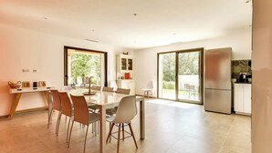 A modern kitchen with a refrigerator, a dining area with a table and chairs, and a view of greenery outside.