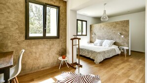 A modern bedroom with a large bed, a standing desk, and a window with a view of trees.