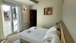 A bedroom with a bed, a bedside table, a lamp, a wooden shelf, and a sliding glass door. - New " Villa Nova " (Cornillon Confoux)
