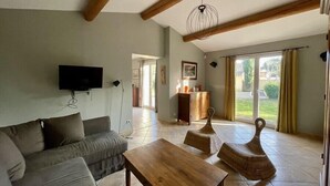 A spacious living room with a sofa, wooden coffee table, and wicker chairs. A television is mounted on the wall, and there is a wooden cabinet with a picture above it. - New " Villa Nova " (Cornillon Confoux)