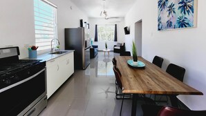 A modern kitchen with a stove, sink, and refrigerator. There is a dining area with a wooden table and chairs. - WE HAVE WATER!! Pool Mansion walk to Beach, sleeps 30+guests (San Juan)