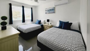 A bedroom with two beds, a ceiling fan, an air conditioning unit, a window with curtains, a small plant, and a painting on the wall. - WE HAVE WATER!! Pool Mansion walk to Beach, sleeps 30+guests (San Juan)