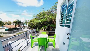 A balcony with green chairs and a table, a white door, and a view of a street and trees. - WE HAVE WATER!! Pool Mansion walk to Beach, sleeps 30+guests (San Juan)