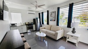 A modern living room with a sofa, a coffee table, a dining table, and a kitchen area with appliances. - WE HAVE WATER!! Pool Mansion walk to Beach, sleeps 30+guests (San Juan)