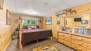 A log cabin-style bedroom with a bed, dresser, and framed pictures on the wall. - Copeland Cabin - Charming Lake House in the Adirondacks (Fort Ann)