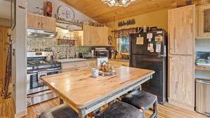 A kitchen with wooden cabinets, a central island, a stove, a refrigerator, and a chandelier. - Copeland Cabin - Charming Lake House in the Adirondacks (Fort Ann)