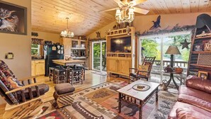 A cozy cabin interior with a wooden ceiling, a dining area, a living room with a sofa and a coffee table, and a kitchen with a refrigerator and cabinets. - Copeland Cabin - Charming Lake House in the Adirondacks (Fort Ann)
