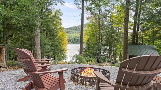 A fire pit with Adirondack chairs in a forested area with a lake view. - Copeland Cabin - Charming Lake House in the Adirondacks (Fort Ann)