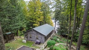 A rustic cabin with a metal roof, surrounded by dense forest and a lake. - Copeland Cabin - Charming Lake House in the Adirondacks (Fort Ann)
