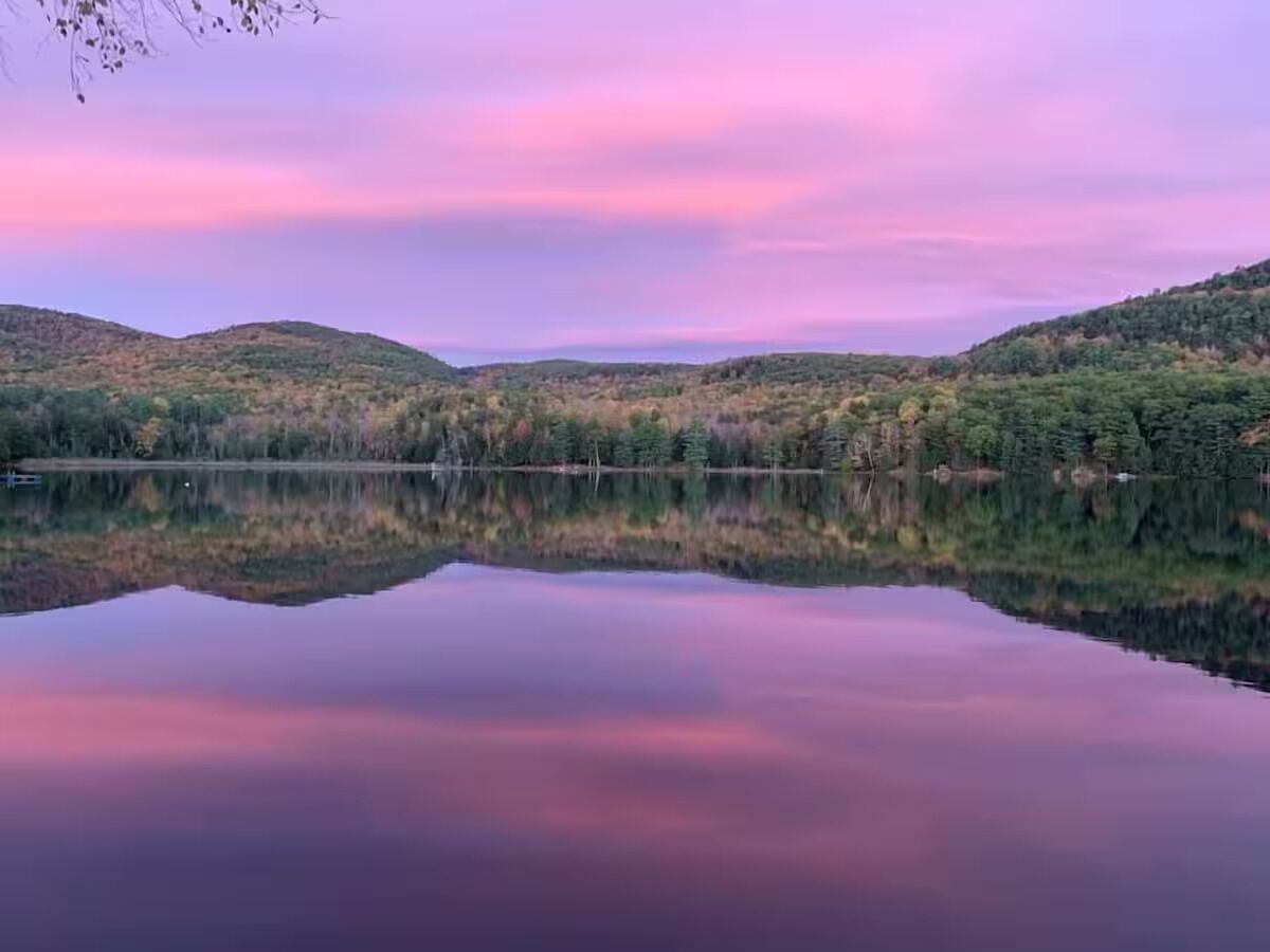 A calm lake with a reflection of the surrounding hills and trees.