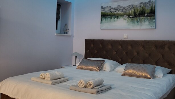 A modern bedroom with a tufted headboard, a painting of a mountain landscape, and a ceiling light. - Charming studio in Zagreb with AC, fitness room, WiFi and spa zone  (Zagreb)