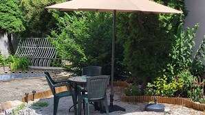 An outdoor patio area with a table and chairs, a large umbrella, and a garden with various plants and a wooden fence. - Charming studio in Zagreb with AC, fitness room, WiFi and spa zone  (Zagreb)