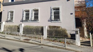 A two-story building with a symmetrical facade, multiple windows with metal bars, and a white fence in front. - Charming studio in Zagreb with AC, fitness room, WiFi and spa zone  (Zagreb)
