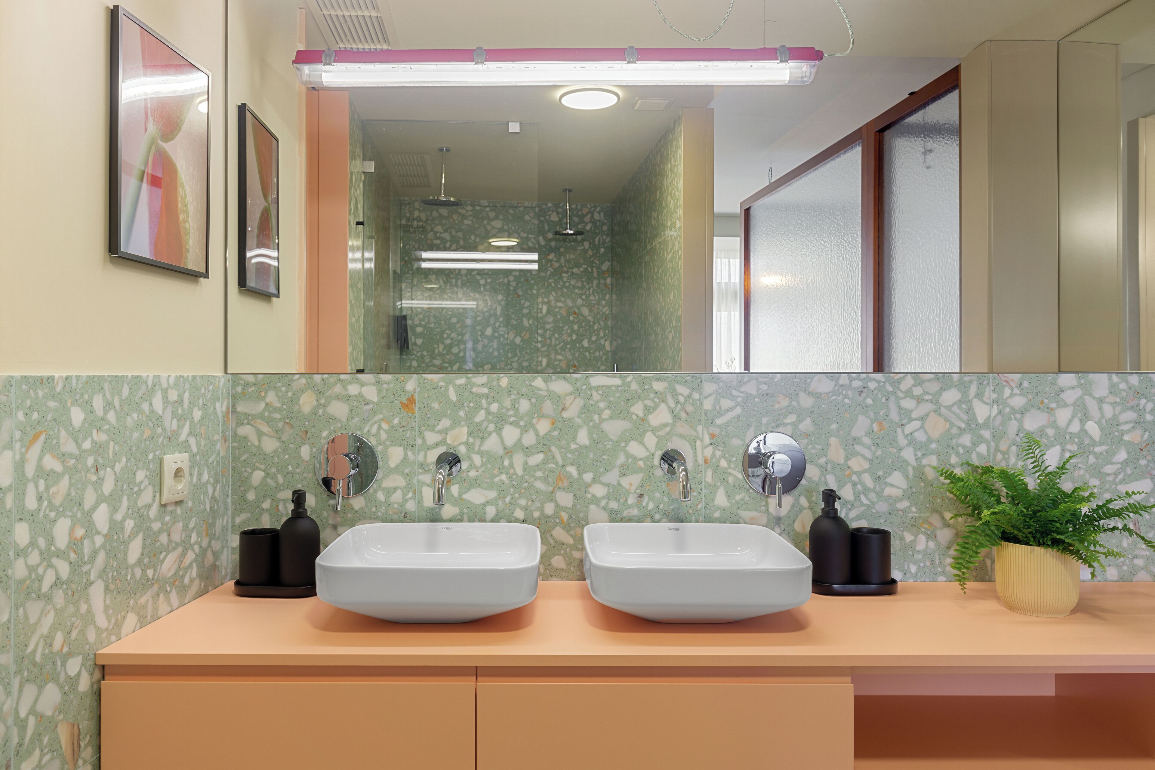 Ein Badezimmer mit zwei Waschbecken, einem Spiegel und einer Pflanze.