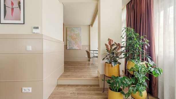Un intérieur moderne avec un escalier menant à un espace repas, de grandes plantes en pot et une œuvre d’art encadrée accrochée au mur.