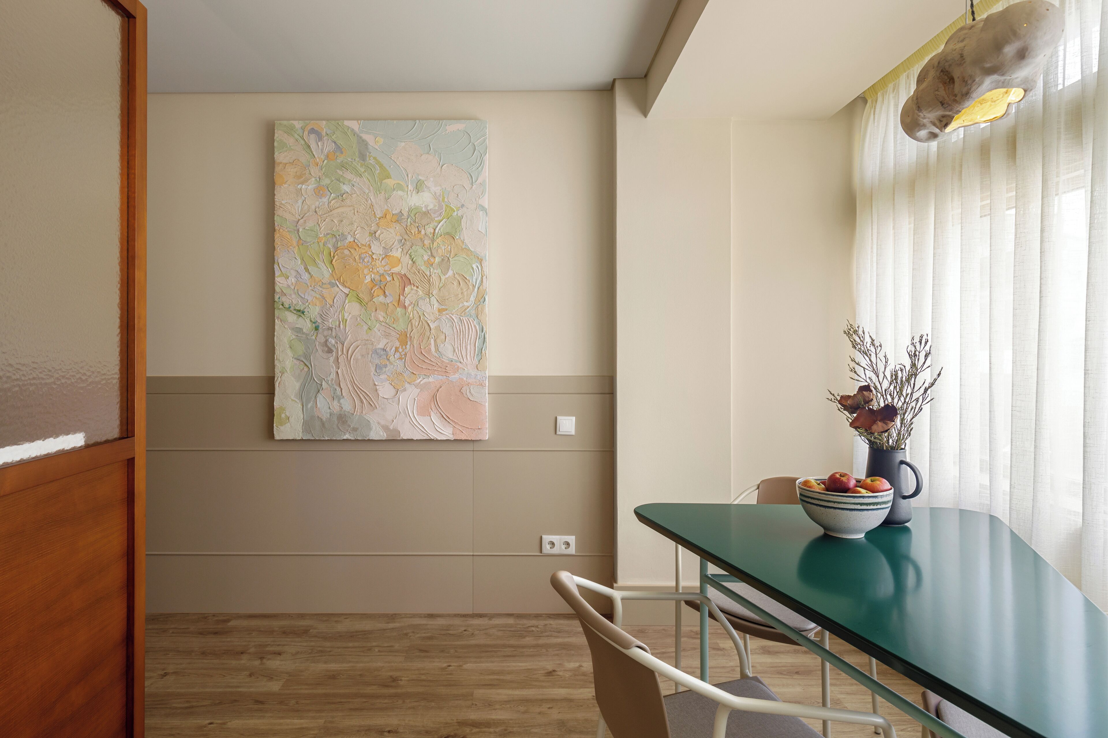 A dining area with a green table, white chairs, a bowl of fruit, and a vase with dried flowers.