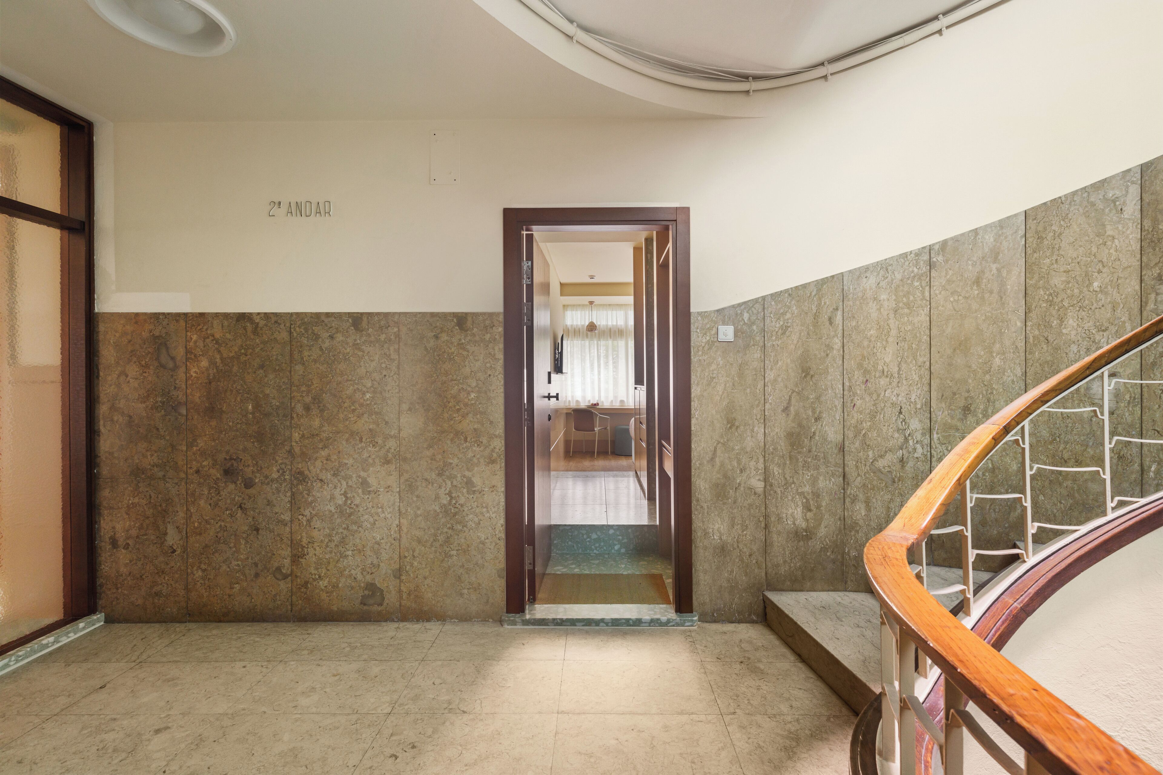 A hallway with a wooden door labeled "2nd ANDAR" leading to a room with a view of a window and a hanging light fixture.