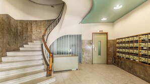 Un intérieur moderne avec un escalier en colimaçon, un comptoir d’accueil et un mur composé de boîtes aux lettres numérotées.