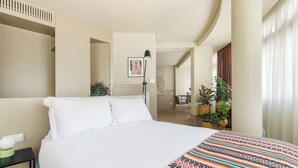 Une chambre d’hôtel avec un grand lit, une table de chevet avec une lampe et une vue sur le couloir.