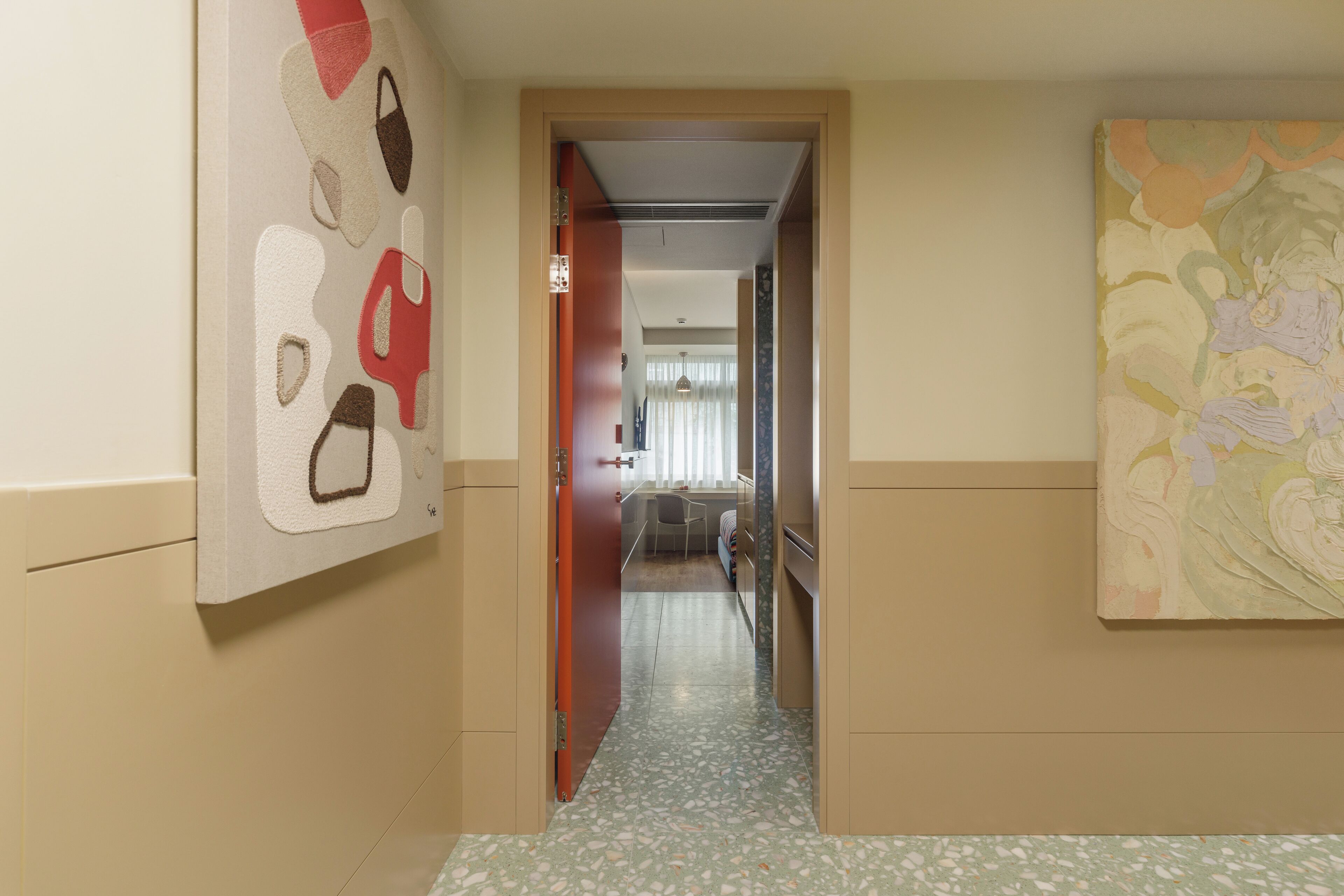 Un pasillo con una puerta que da a una habitación, un cuadro en la pared y un suelo estampado.