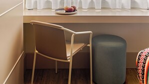 Une pièce avec une fenêtre, une chaise, un petit pouf et un luminaire suspendu.