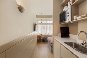 A compact kitchen with a microwave, sink, and a small dining area with a chair and table. - Pelicano (Porto)
