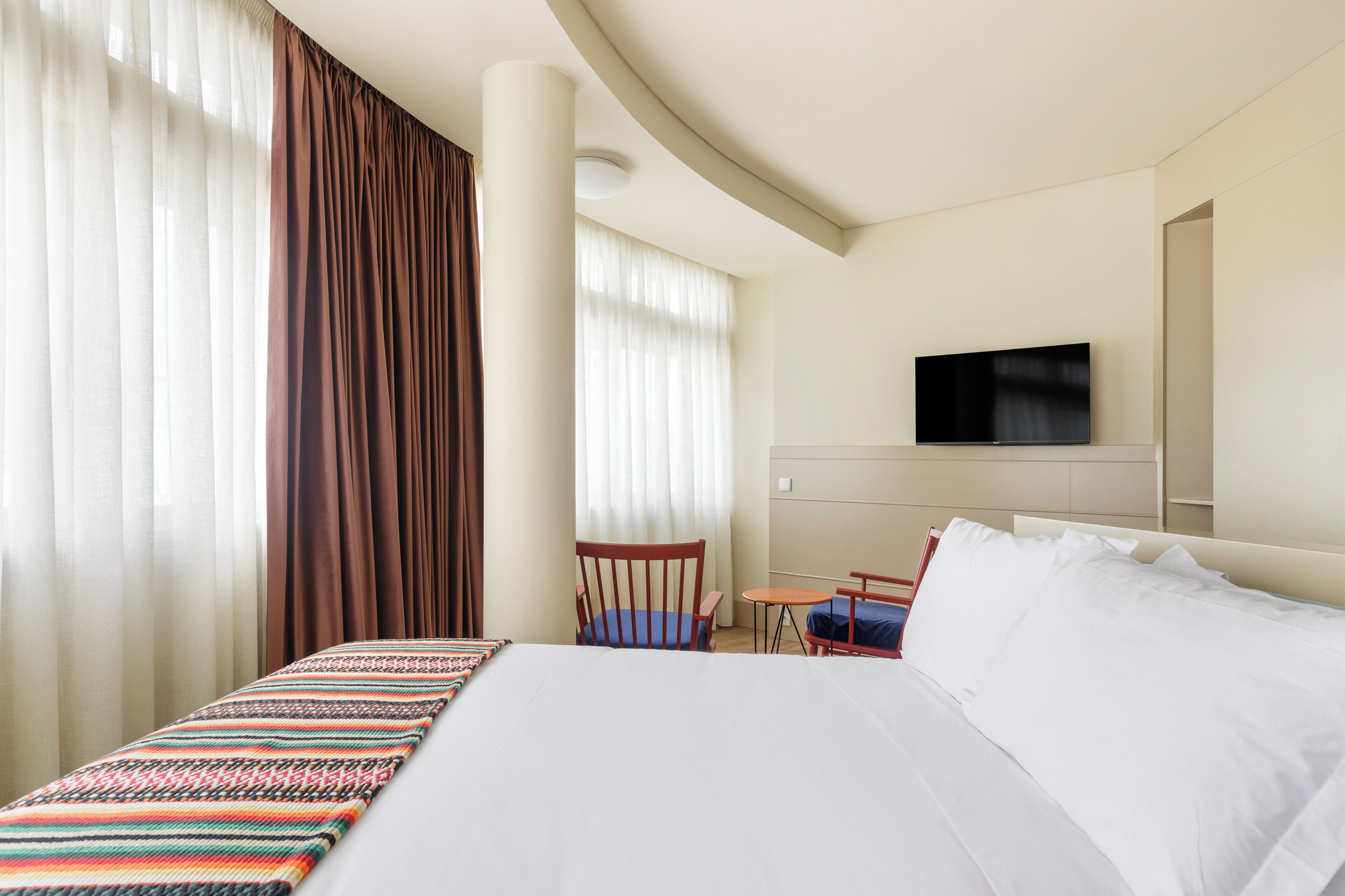Una habitación de hotel con una cama grande, un televisor montado en la pared, una silla y una mesita.