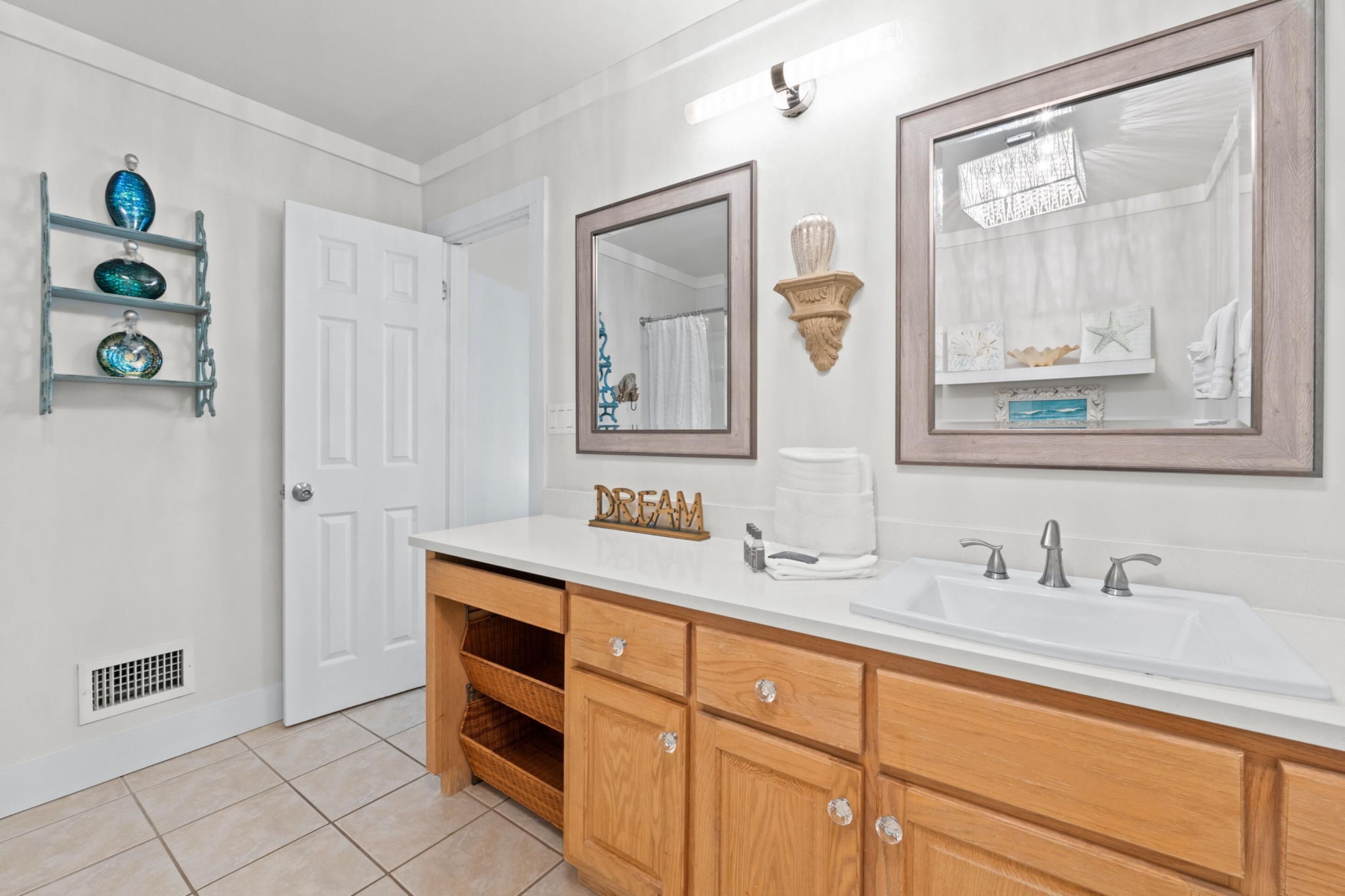 Une salle de bain avec un meuble-lavabo blanc, deux vasques, des armoires en bois, un porte-serviettes et des objets décoratifs accrochés au mur.
