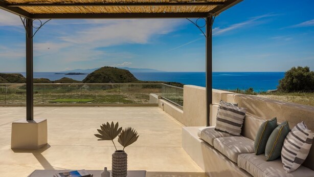 A covered outdoor seating area with a view of the sea, a concrete floor, and a sofa with cushions. - Villa Lobelia - Ionian Villa Collection (Lixouri)