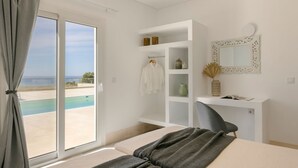 A bedroom with a large sliding glass door leading to a pool, a white desk with a mirror, and a gray chair. - Villa Lobelia - Ionian Villa Collection (Lixouri)