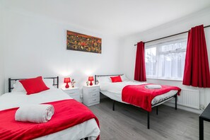 Ett hotellrum med två sängar, rött sänglinne, en tavla på väggen och ett fönster med röda gardiner.
