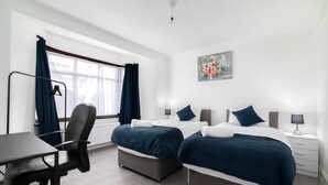 A hotel room with two beds, a desk, a chair, and a window with curtains. - Refurbished 4-bed Family Home-near Central London (London)