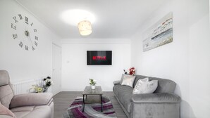A modern living room with a grey sofa, a coffee table, a wall clock, a flat-screen TV displaying 'NETFLIX', and a painting on the wall. - Refurbished 4-bed Family Home-near Central London (London)