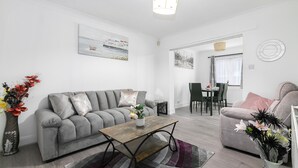 A modern living room with a grey sofa, a wooden coffee table, and a dining area in the background. - Refurbished 4-bed Family Home-near Central London (London)