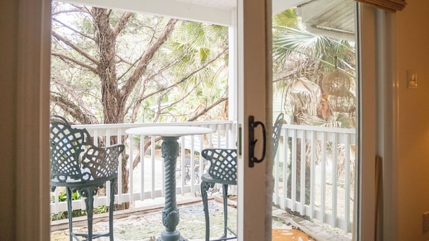 A covered outdoor seating area with a table and chairs, a white fence, and a tree in the background. - 2BR/2.5BA in the PERFECT location in Ocean Springs! Downtown Sanctuary (Ocean Springs)