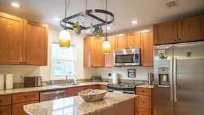 A modern kitchen with wooden cabinets, granite countertops, stainless steel appliances, and pendant lighting. - 2BR/2.5BA in the PERFECT location in Ocean Springs! Downtown Sanctuary (Ocean Springs)