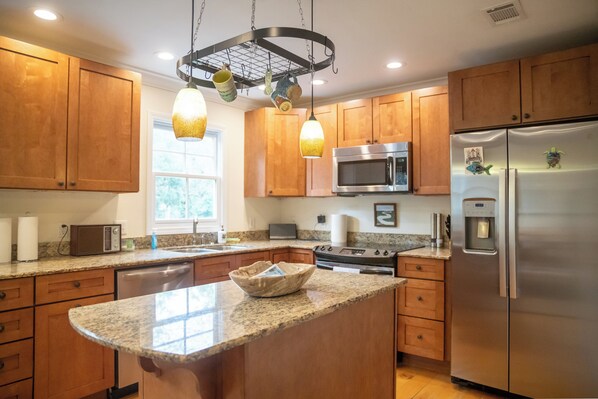 A modern kitchen with wooden cabinets, granite countertops, stainless steel appliances, and pendant lighting. - 2BR/2.5BA in the PERFECT location in Ocean Springs! Downtown Sanctuary (Ocean Springs)