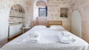 A stone-walled bedroom with a wooden bed, a small window, and a white radiator.