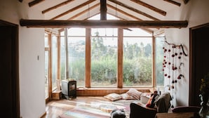 A rustic room with a large window, wooden beams, a cozy seating area, and a small heater. - Country house in the middle of nature. (Chinchero)
