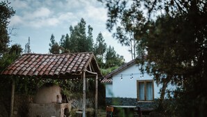 A rustic outdoor setting with a stone oven, a wooden structure with a tiled roof, and a house with a stone foundation and a window. - Country house in the middle of nature. (Chinchero)