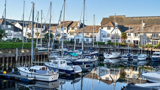Un port de plaisance où sont amarrés de nombreux bateaux, entouré d’immeubles résidentiels à l’architecture traditionnelle.