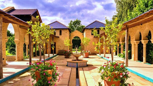 Un patio con arcos, plantas en macetas y una fuente central.