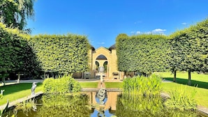 Un jardín tranquilo con un estanque central, un puente de piedra y un edificio con una entrada arqueada.