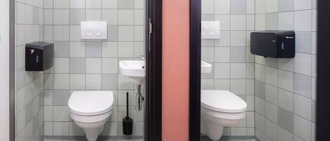 A modern bathroom with two toilets, a sink, and two soap dispensers.