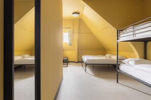 A dormitory room with bunk beds, a small table, and a window with curtains.