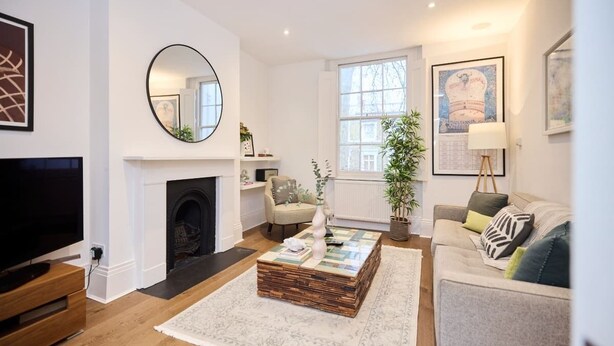 A modern living room with a fireplace, a television, a round mirror, and a large window. - The Chelsea Classic - Splendid 3bdr House With Terrace (London)