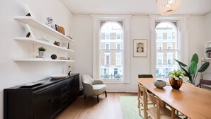 A modern kitchen with white shelves, a wooden dining table, and large windows. - The Chelsea Classic - Splendid 3bdr House With Terrace (London)